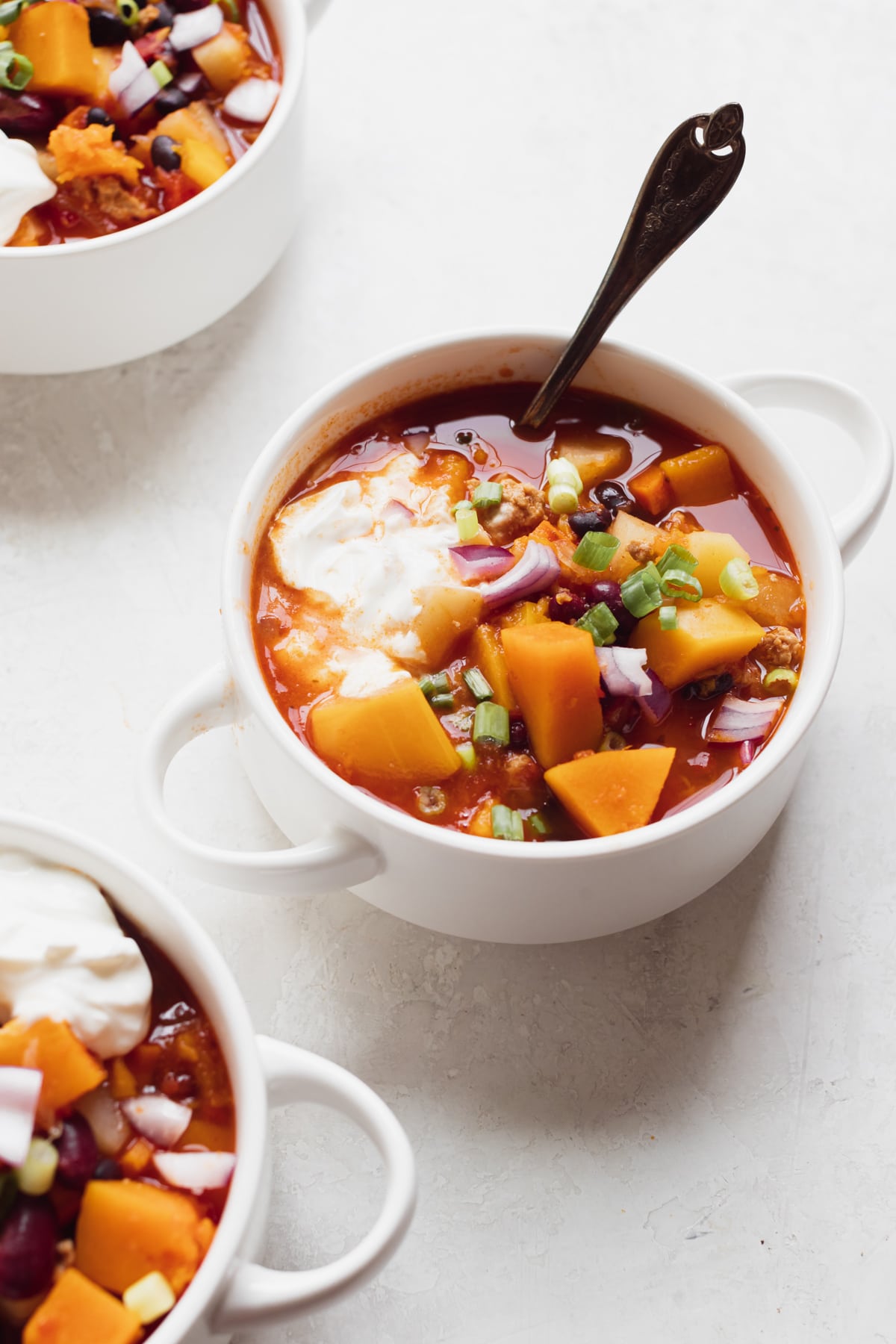 chili in a white soup bowl topped with green onions and sour cream