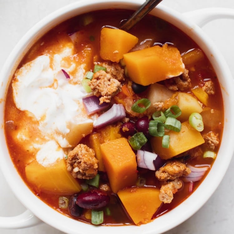chili in a white soup bowl topped with green onions and sour cream