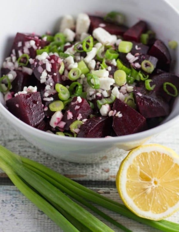 Chopped roasted beets on a wood board topped with feta cheese and green onions.