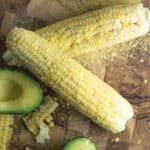 2 ears of corn on the cob covered in nutritional yeast with half an avocado next to them