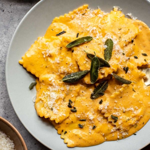 a gray plate with raviolis in a pumpkin alfredo sauce topped with fresh sage