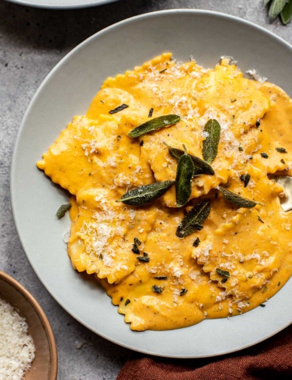 a gray plate with raviolis in a pumpkin alfredo sauce topped with fresh sage