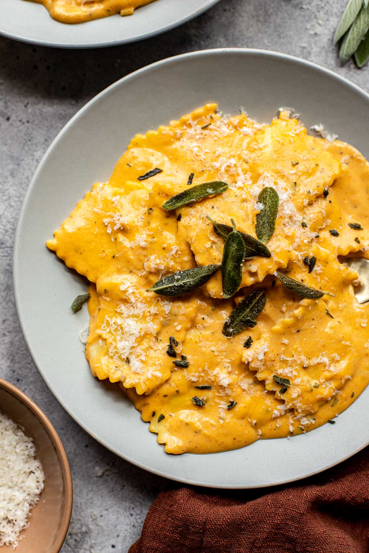 a gray plate with raviolis in a pumpkin alfredo sauce topped with fresh sage
