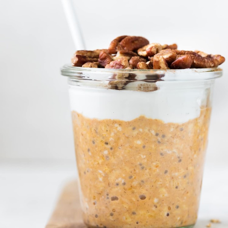 overnight oats made with pumpkin puree in a glass jar topped with Greek yogurt, chopped pecans and ground cinnamon