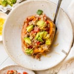 a sweet potato in a bowl stuffed with ground turkey and topped with avocado and cheese