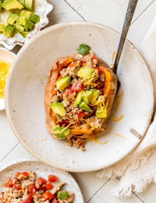 a sweet potato in a bowl stuffed with ground turkey and topped with avocado and cheese
