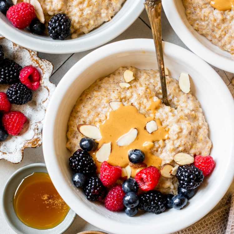 steel cut oatmeal in white bowls topped with peanut butter and fresh berries.