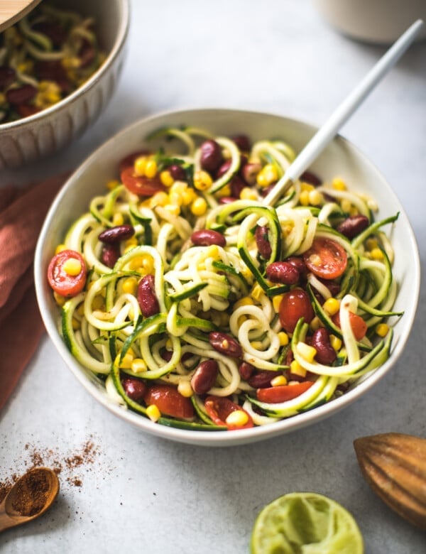 zoodle salad in a large white bowl with corn, tomatoes and kidney beans