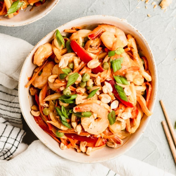 noodles in a white bowl with peanut sauce and shrimp garnished with green onions