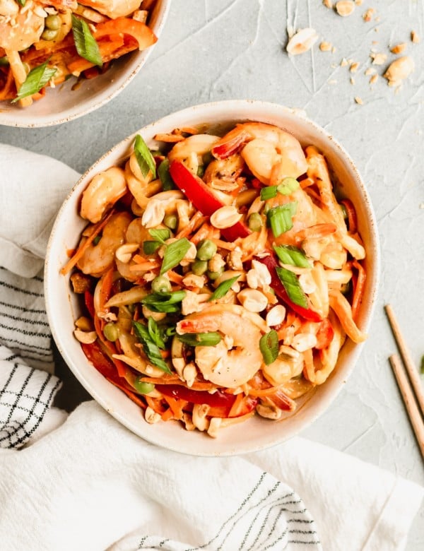 noodles in a white bowl with peanut sauce and shrimp garnished with green onions