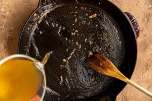 broth being poured into black cast iron skillet to deglaze the pan