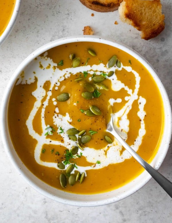 butternut squash soup in a white bowl garnished with heavy cream and pepitas