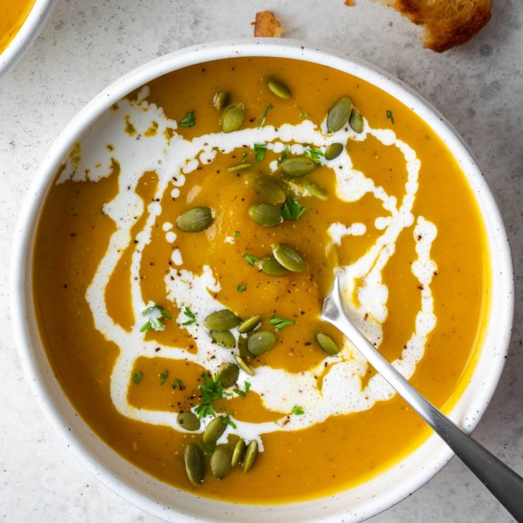 butternut squash soup in a white bowl garnished with heavy cream and pepitas
