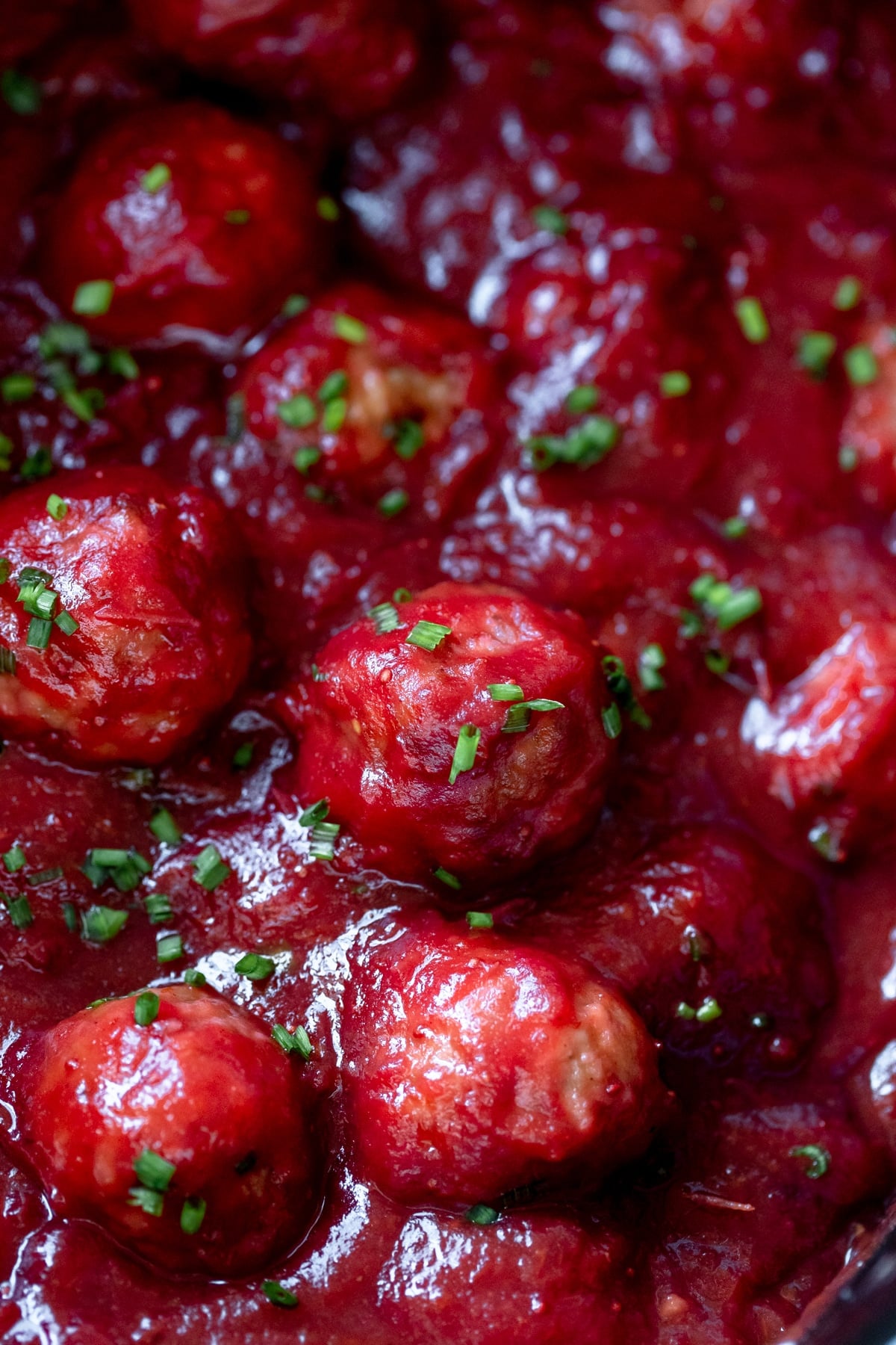 an up close image of meatballs covered in cranberry sauce and garnished with chives in a cast iron skillet