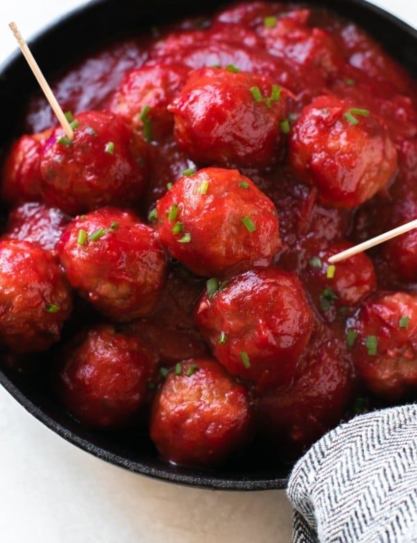 meatballs covered in cranberry sauce and garnished with fresh chives in a cast iron skillet with toothpicks