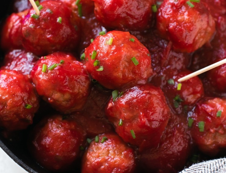 meatballs covered in cranberry sauce and garnished with fresh chives in a cast iron skillet with toothpicks