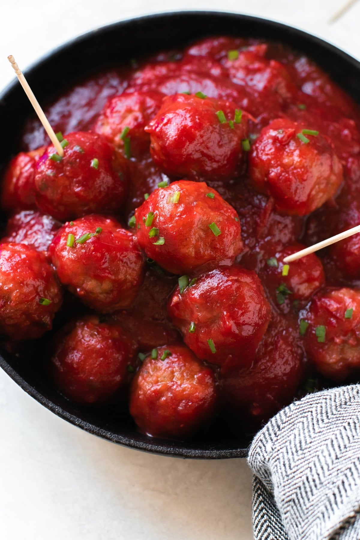 meatballs covered in cranberry sauce and garnished with fresh chives in a cast iron skillet with toothpicks