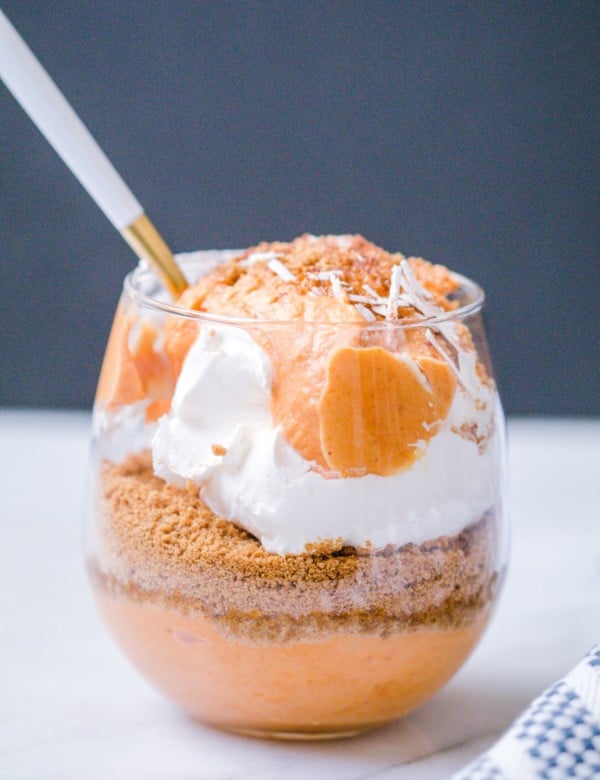 Pumpkin pie parfait layered with pumpkin pie yogurt mixture, ginger snap cookies and cool whip in a wine glass.