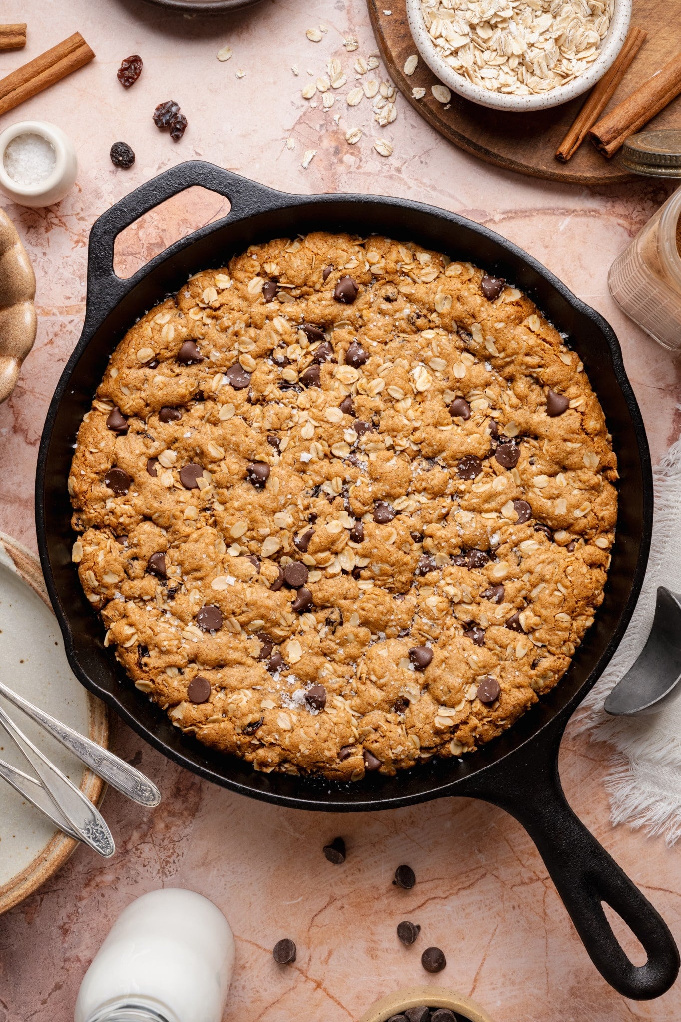 An overhead view of a freshly baked oatmeal raisin chocolate chip cookie skillet in a black cast iron pan, showing a golden surface with oats and chocolate chips scattered throughout.
