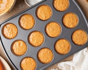 Carrot cake muffin batter divided evenly into paper-lined muffin tin cups, filled nearly to the top.