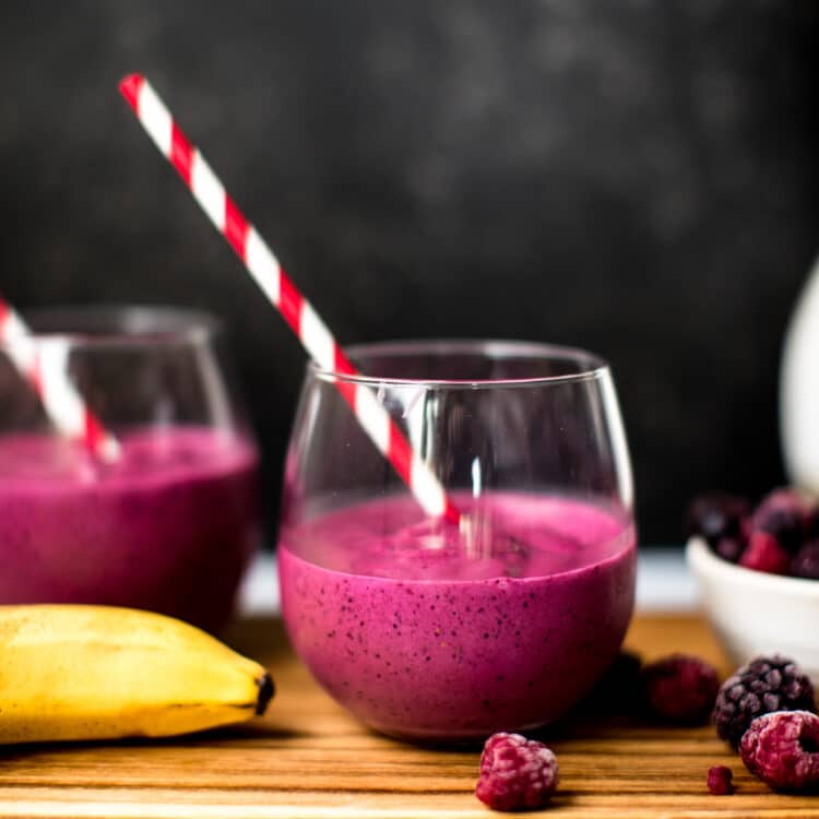 a blueberry beet smoothie in a wine glass with a red straw