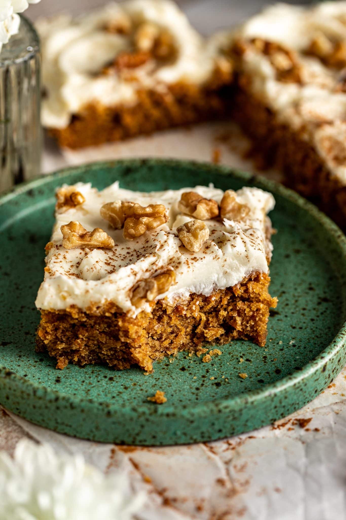 Close-up of a carrot cake bar with a bite taken out, revealing moist crumb texture, cream cheese frosting, and walnut topping.