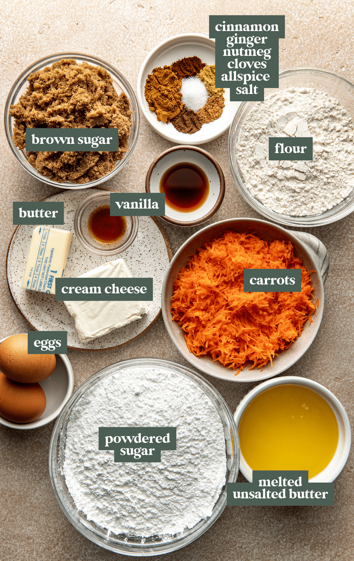 Flat lay of ingredients for carrot cake bars including shredded carrots, brown sugar, melted butter, eggs, cream cheese, flour, spices, vanilla, and powdered sugar.
