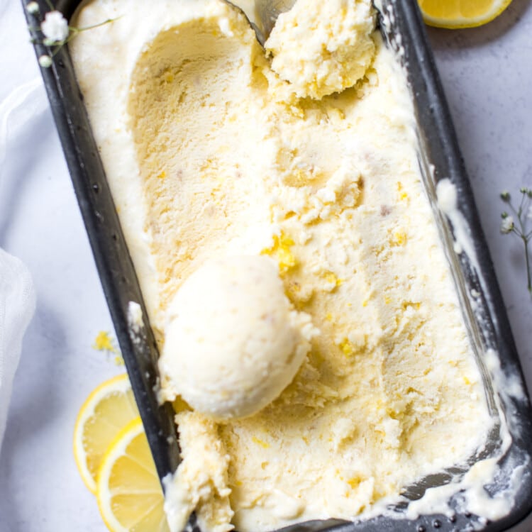 lemon ice cream in a container being scooped with an ice cream scooper