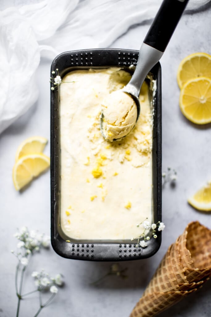 lemon ice cream in a container being scooped with an ice cream scooper