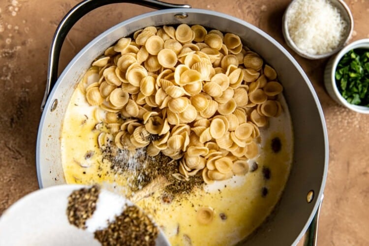 adding spices and dry pasta to liquid mixture in dutch oven pan