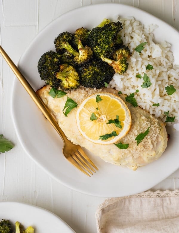 chicken breast on a white plate with roasted broccoli, white rice and a gold fork