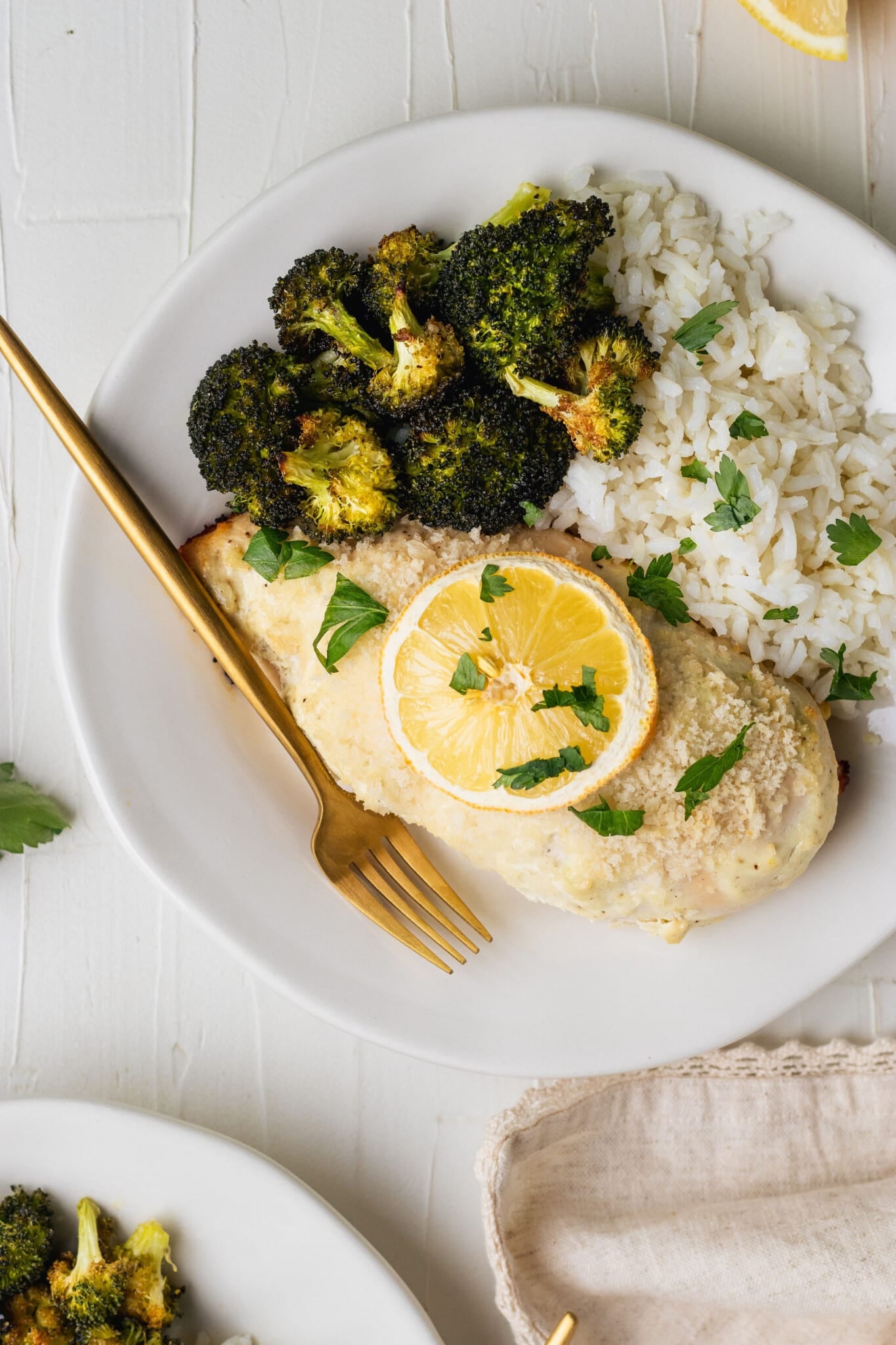 chicken breast on a white plate with roasted broccoli, white rice and a gold fork
