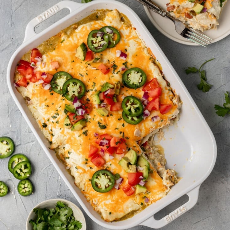 white dish with a mexican casserole inside & a piece missing, topped with avocado, tomatoes, and shredded cheese