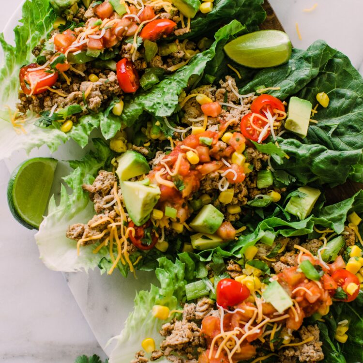 three romaine lettuce leaves filled with a ground turkey mixture with avocado, shredded cheese, corn, and salsa