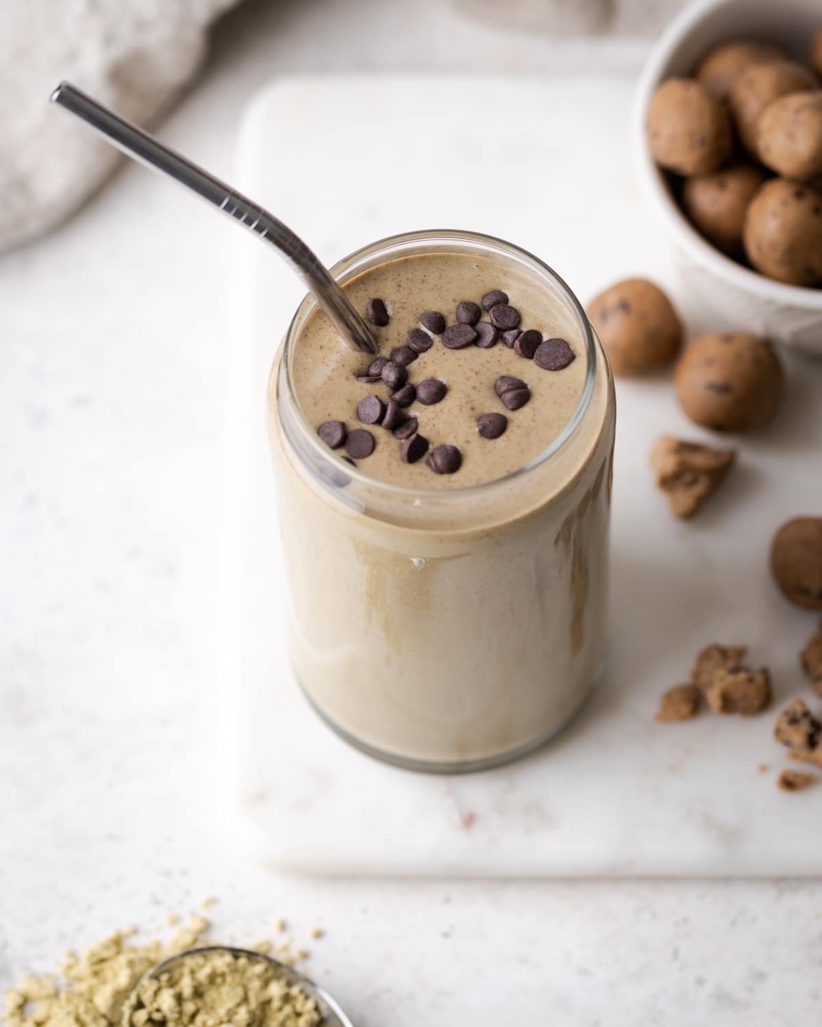 a smoothie in a glass cup with a metal straw in it with chocolate chips on top