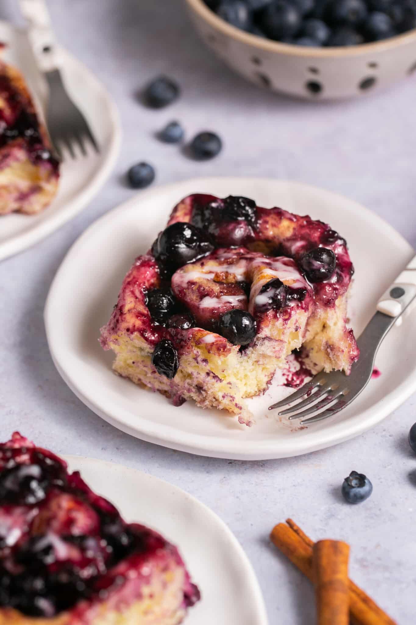 A cinnamon roll on a a plate with blueberry sauce on top. 