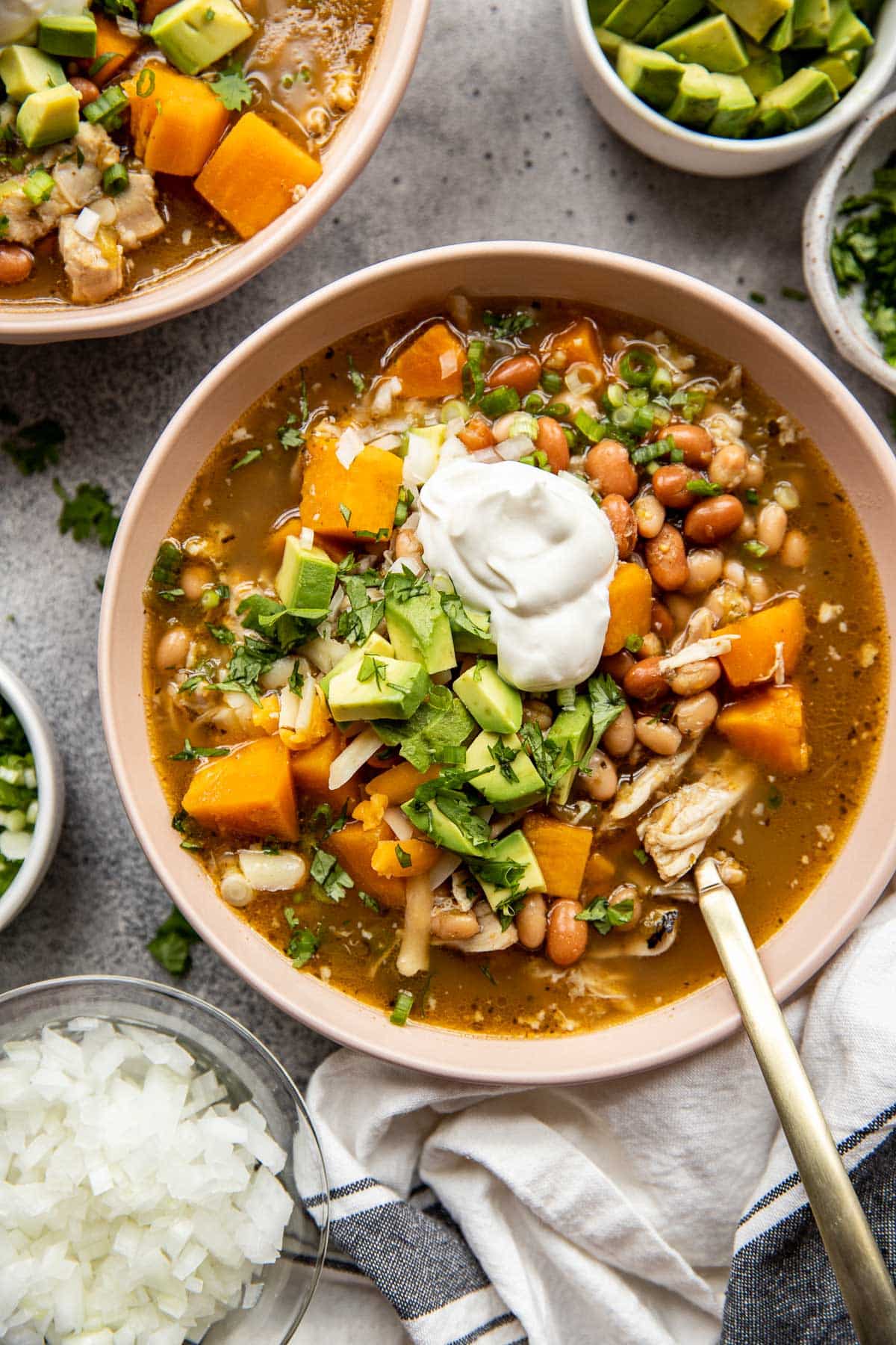tan bowl of chicken chili soup topped with avocado and sour cream