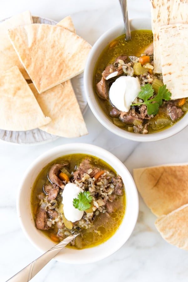 chicken shawarma soup in white bowls topped with sour cream and cilantro with pita bread on the site