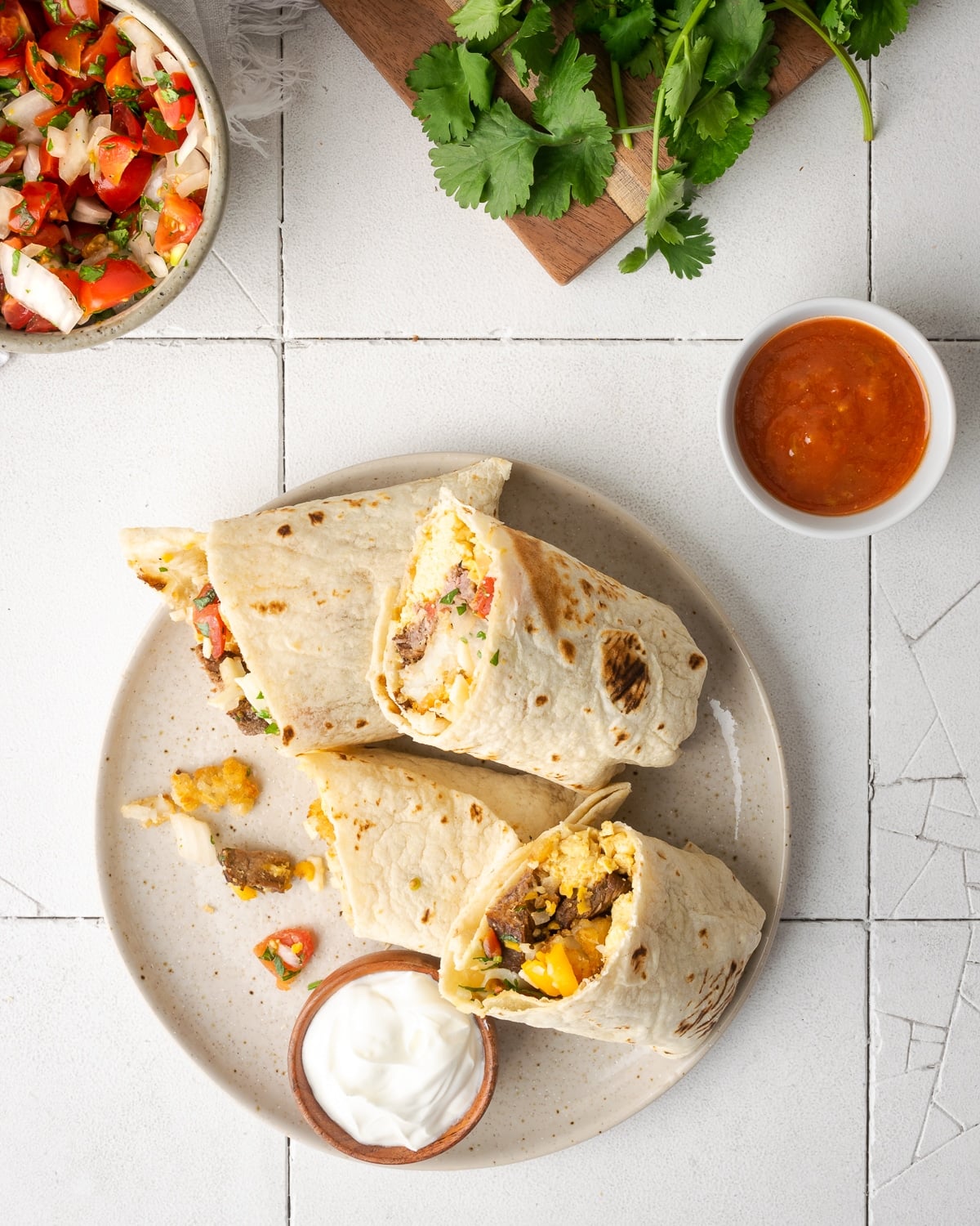 breakfast burritos on a white speckled plate with sour cream on the side