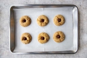 six almond butter blossom cookies on a baking tray with candy kisses inserted on top
