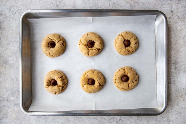 six almond butter blossom cookies on a baking tray with candy kisses inserted on top