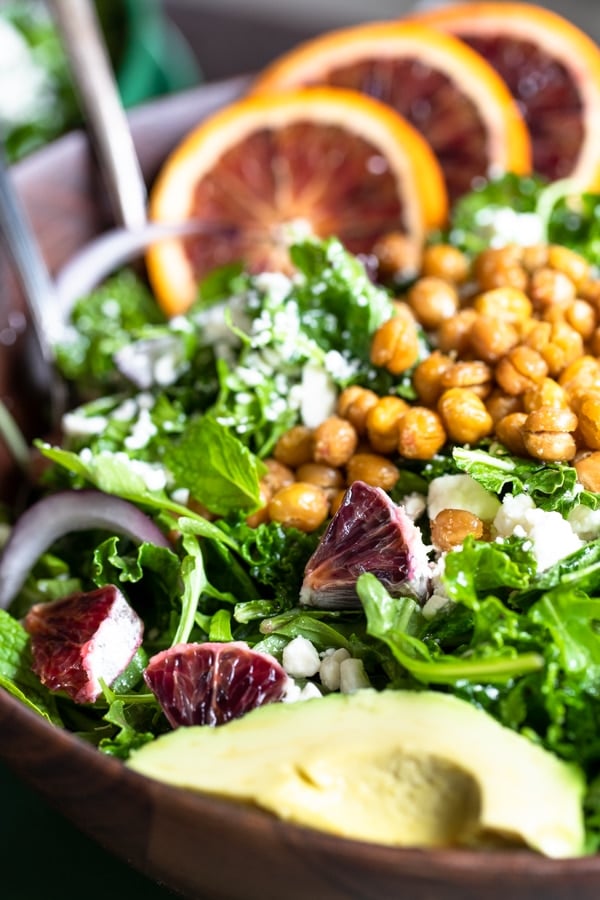 a green salad in a wooden bowl topped with chickpeas, avocado and blood oranges