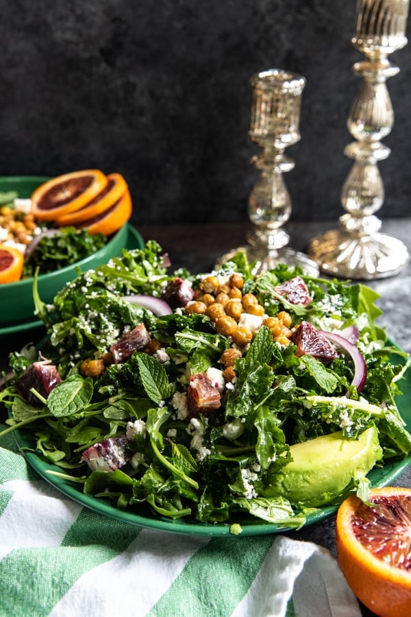 a winter blood orange salad with massaged kale and arugula on a green plate topped with mint and chickpeas