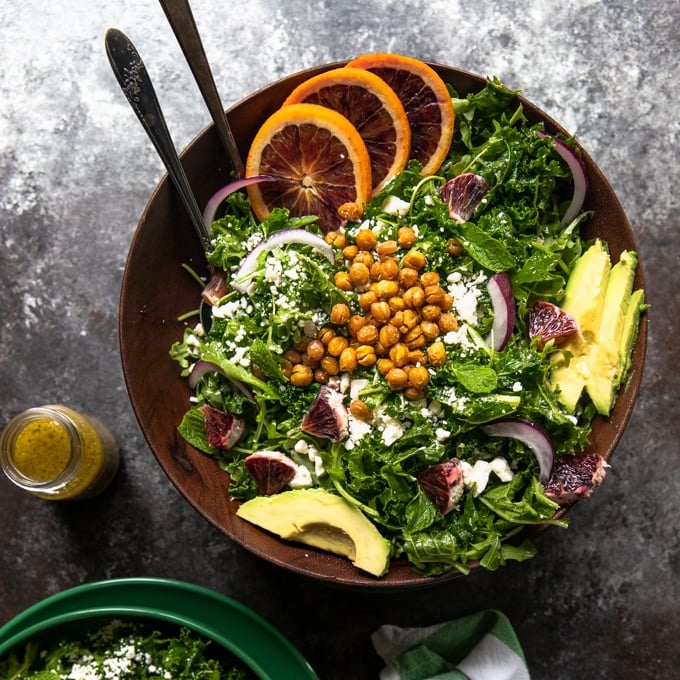 a green salad in a wooden bowl topped with chickpeas, avocado and blood oranges