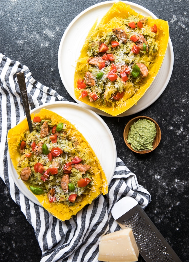 spaghetti squash boats filled with chicken sausage, vegan avocado pesto and topped with cherry tomatoes and basil on white plates