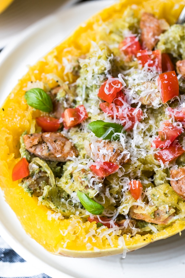 spaghetti squash boats filled with chicken sausage, vegan avocado pesto and topped with cherry tomatoes and basil on white plates