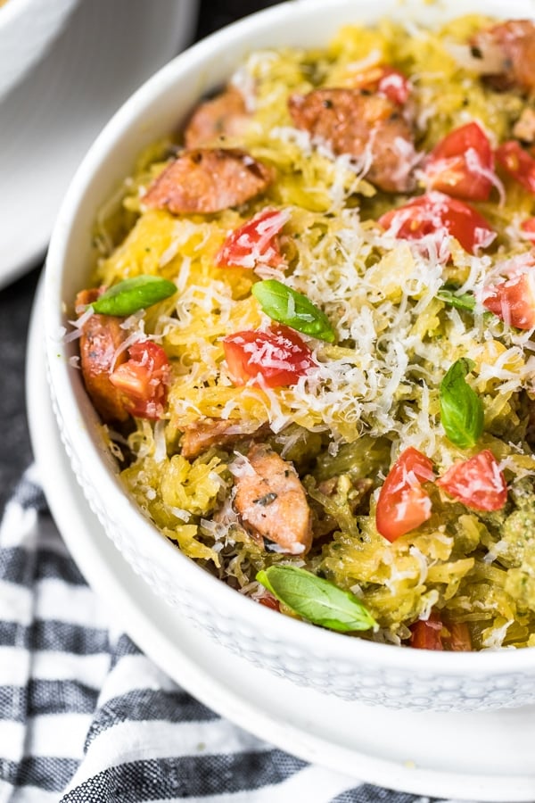 spaghetti squash boats filled with chicken sausage, vegan avocado pesto and topped with cherry tomatoes and basil in a white bowl