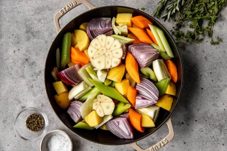 black dutch oven full of uncooked chopped vegetables and garlic