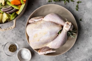 raw whole chicken on a plate with herbs