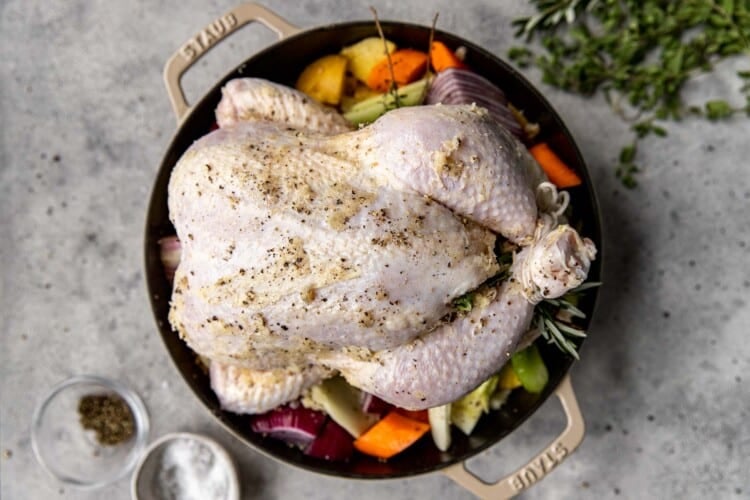 raw full chicken surrounded by vegetables in a black dutch oven pot